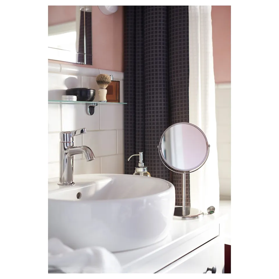 Bathroom with white sink, chrome tap, round magnifying mirror, black patterned shower curtain.