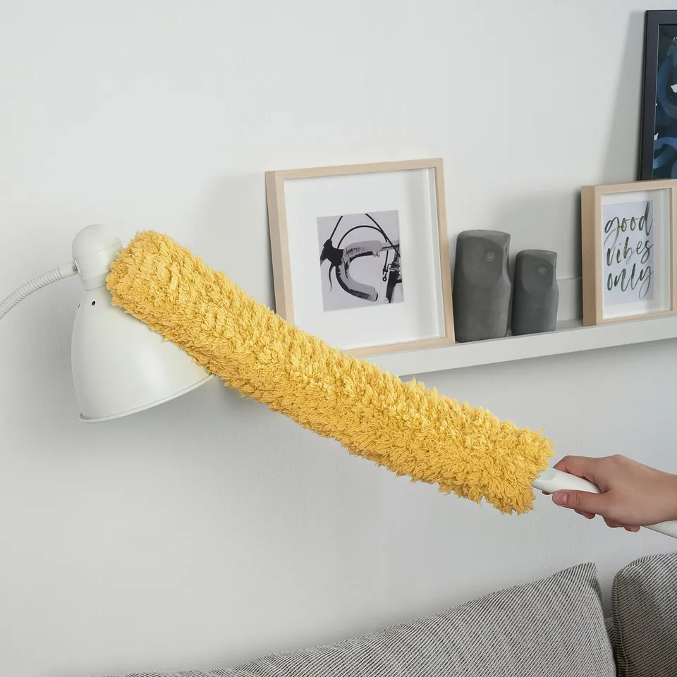 Hand holds yellow duster cleaning, with pictures on wall.