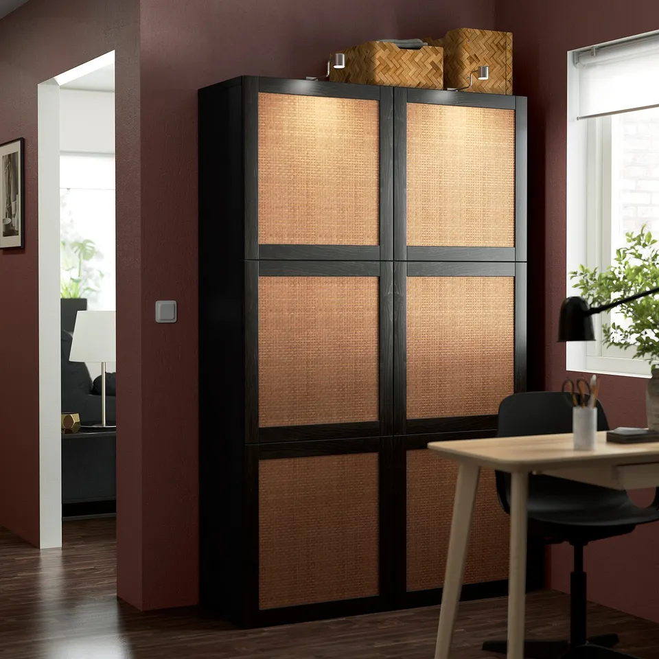 Large ikea BESTÅ storage unit in black/beige with woven doors next to desk/chair in office.