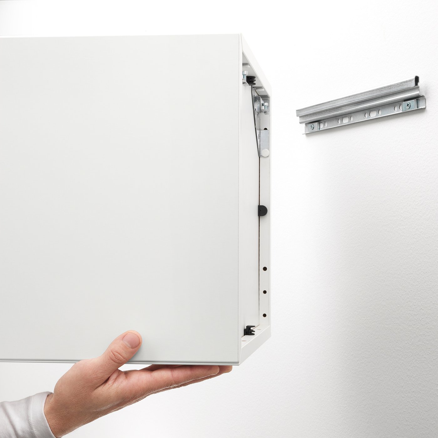 Hand holding wall-mountable EKET cabinet, highlighting its storage and space-saving design.