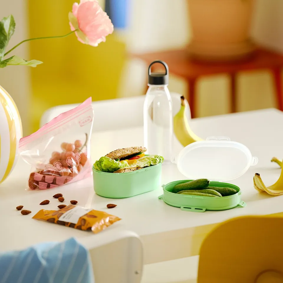 Mint green lunch box with sandwich, pickles, grapes, and nuts.