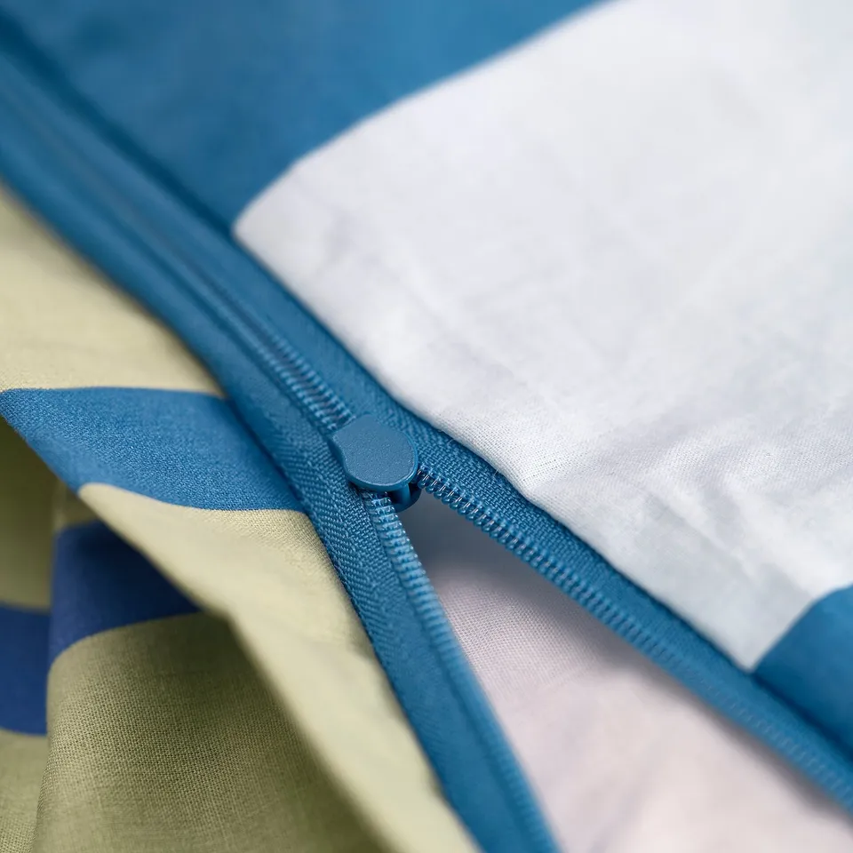 A close-up of a blue zip on a light blue and white blanket, showing its functionality.