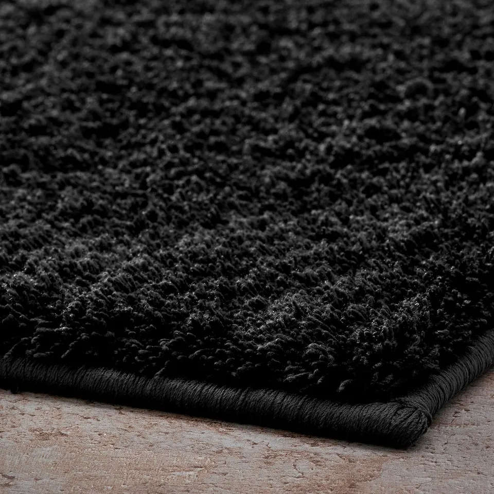 Soft, black bath mat on a tiled floor. Thick, plush texture for comfort.