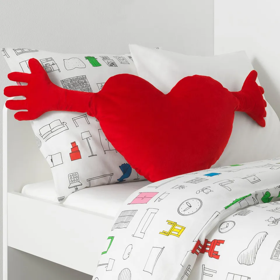 Heart-shaped pillow on bed, symbolising love, likely childrens room, soft and huggable.