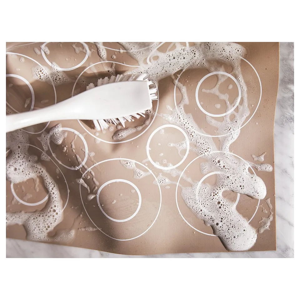 Top view of a white silicone baking mat with circular patterns for cookies or pastries, featuring a brush.