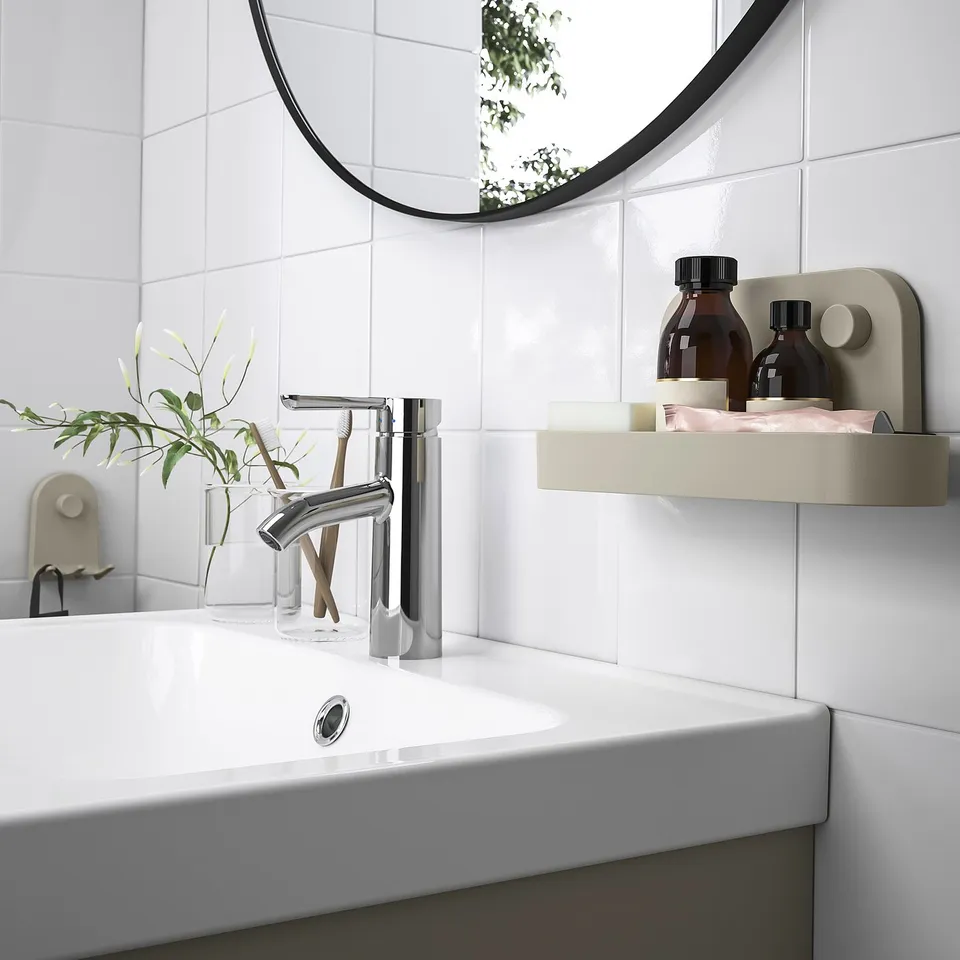 Modern bathroom with white øbonäs organisers: gray-beige shelves hold bottles, a plant, and toiletries next to a white sink and round mirror.