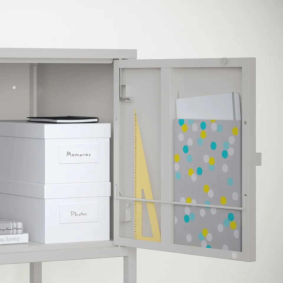 White storage cabinet with open door. Visible are boxes labelled memories and photos, a laptop, and a bulletin board with colourful polka dots.