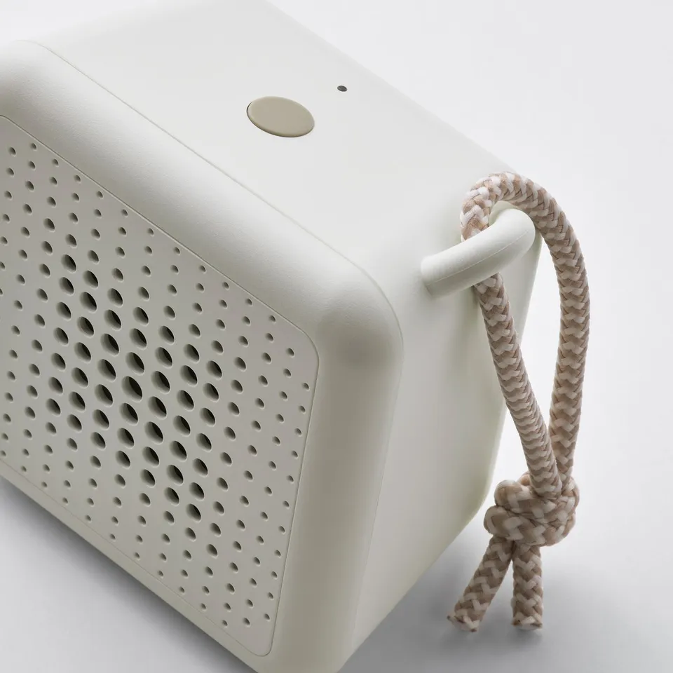Portable speaker with a woven rope handle, dot-patterned speaker grill. Modern, compact design.