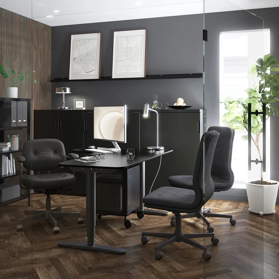 Modern office with black furniture, computer, plants, and artwork on dark floors.
