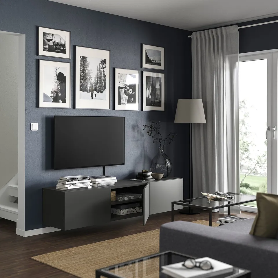 Modern living room with dark grey wall, black tv, and framed photos. Glass coffee table with magazines, grey curtain, and wooden floor.