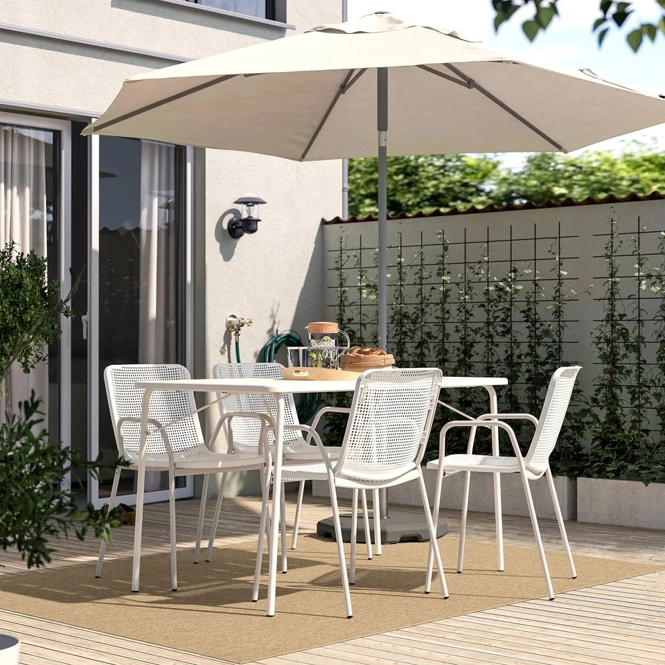 Beige outdoor rug under white patio set with house and greenery.