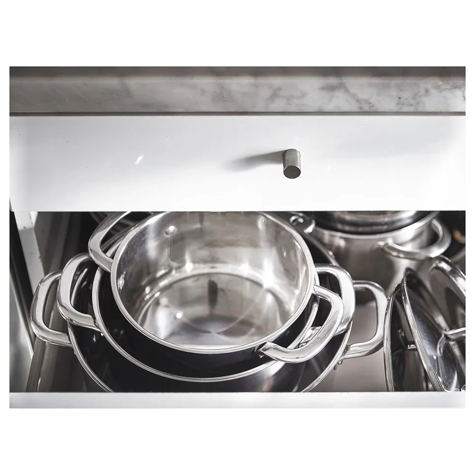 Stacked stainless steel pots with handles, stored neatly under a white drawer.