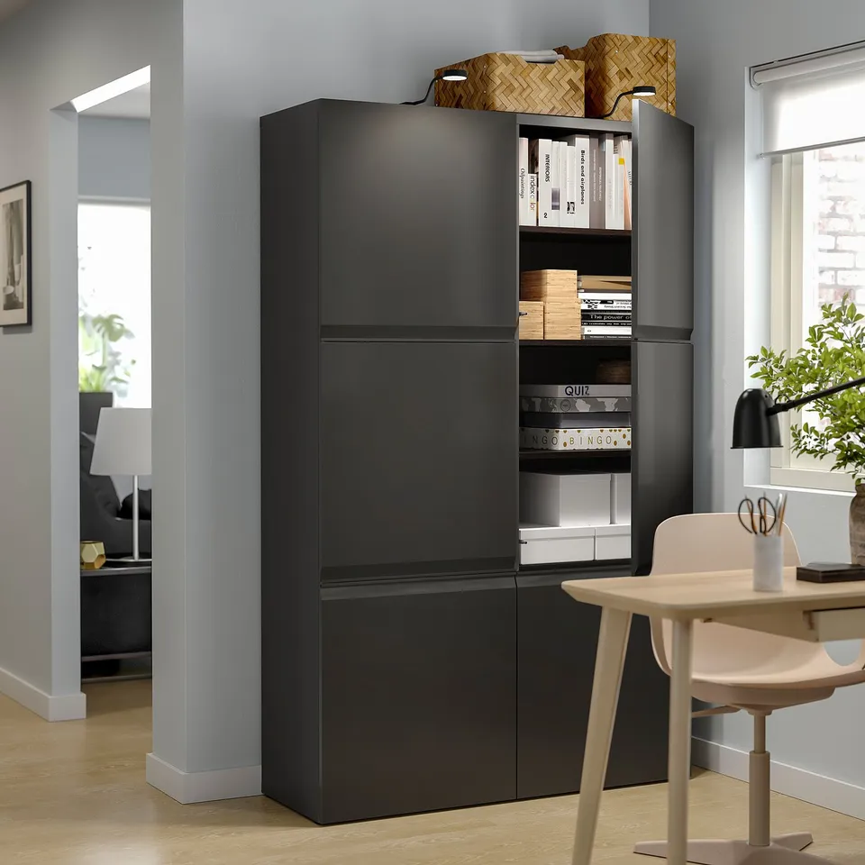 Modern living room with black BESTÅ storage unit, housing books and games. Accented by a beige chair and plant.