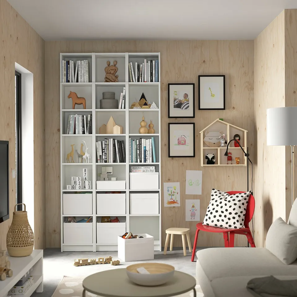 Cosy kids room with white BILLY bookcase, red chair, wooden decor, toys, and art on light wooden walls.