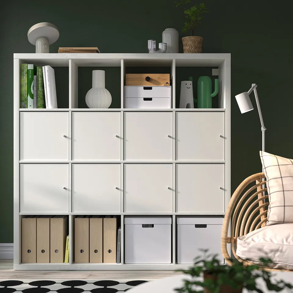 KALLAX shelving with books, vases, plants, and a wicker chair with a lamp beside it.