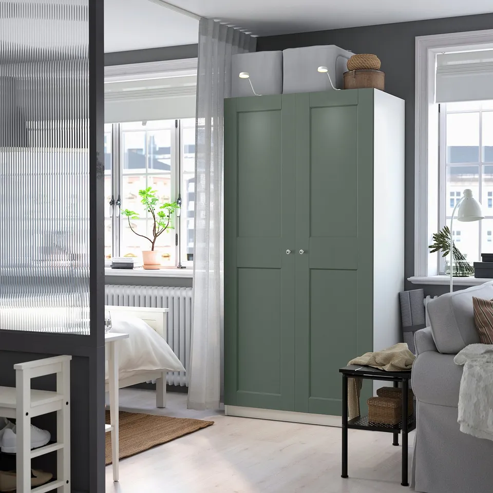 Modern bedroom with tall greenish-gray PAX wardrobe, large window, grey sofa, and white bed.