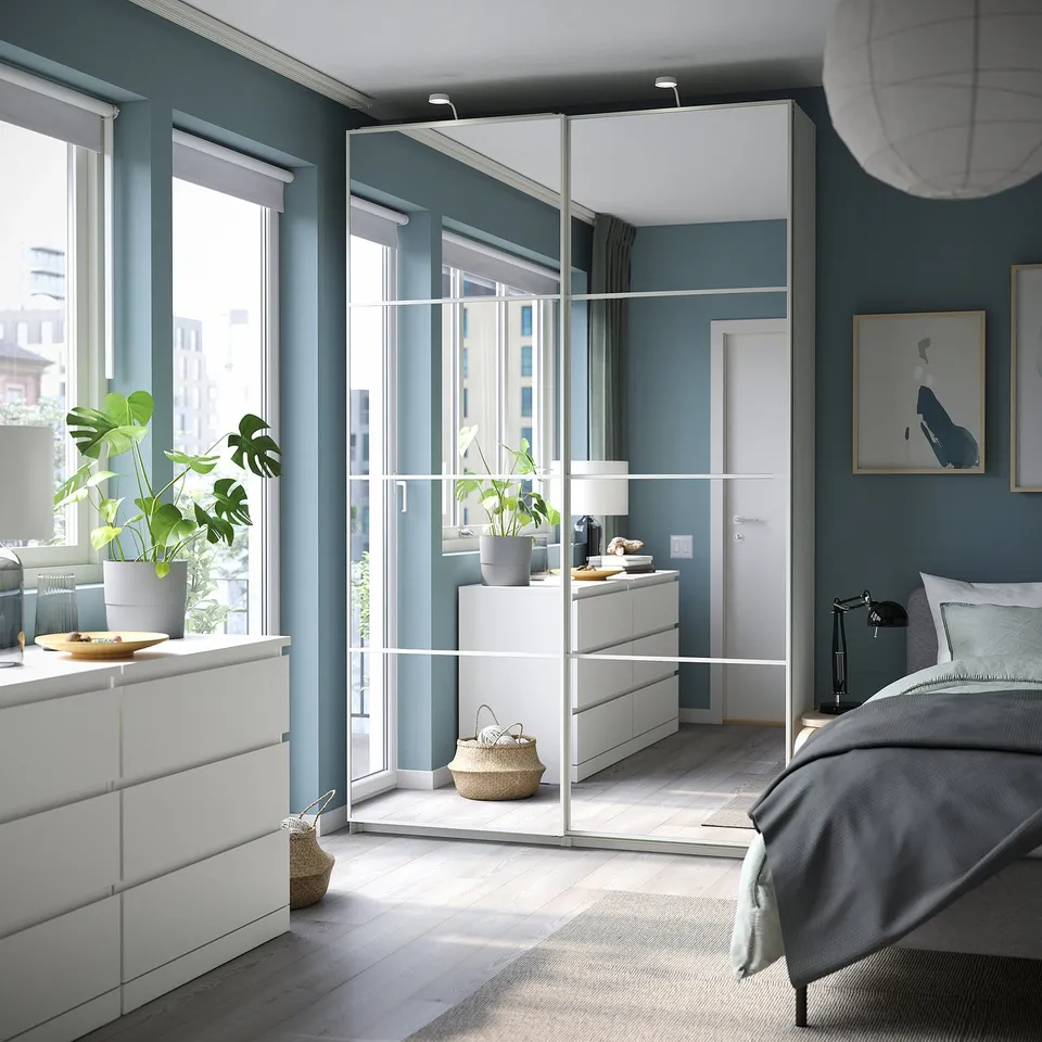 Modern bedroom with white PAX wardrobe, mirrored doors, wooden floors, grey bedding.