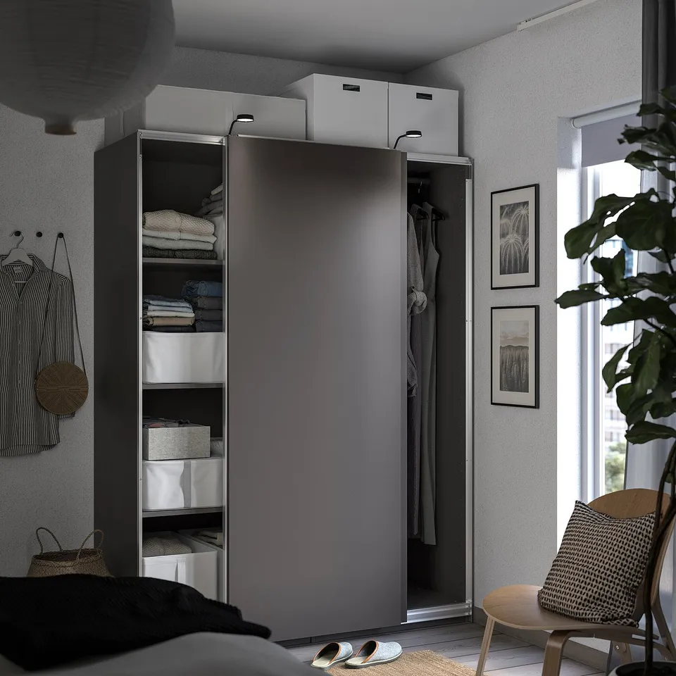 Modern bedroom with grey PAX wardrobe, clothes visible, chair by window and plant.