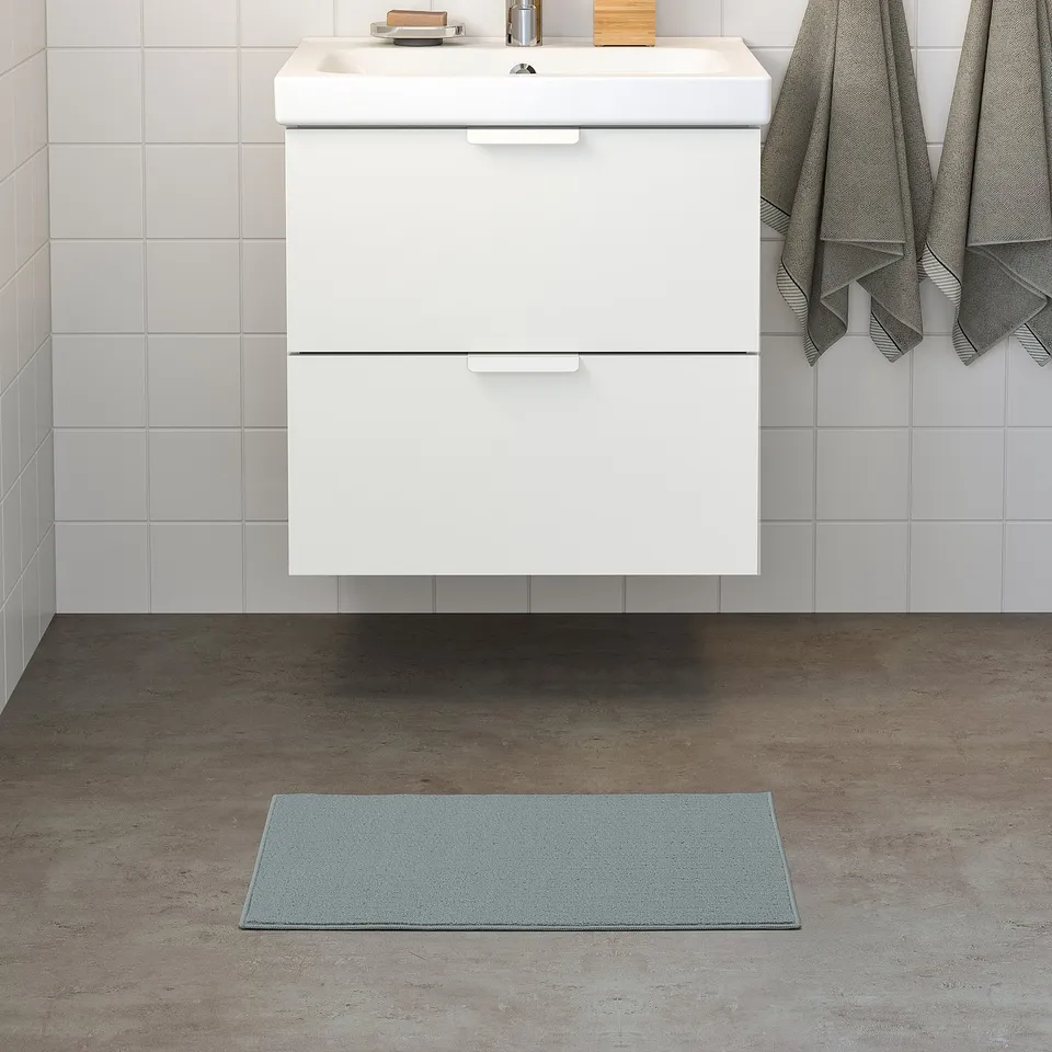 Modern bathroom with blue FINTSEN mat beside white vanity, fitting under.