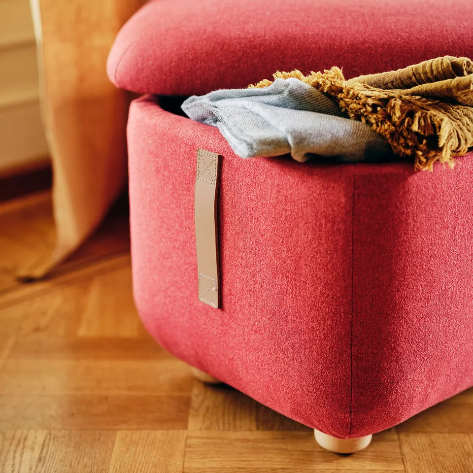 Red fabric ottoman with storage, folded blanket visible, on wooden floor.