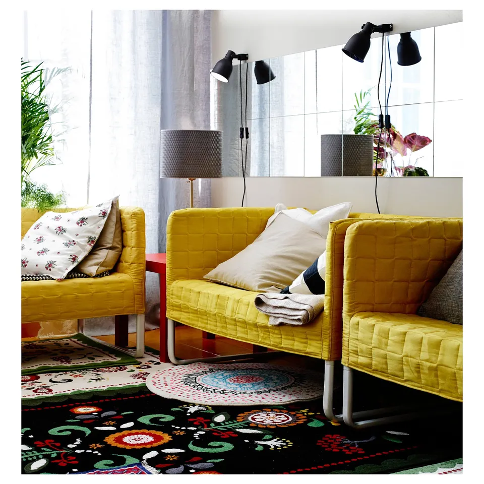 Bright living room with yellow armchairs, colourful floral rug, and large wall mirror.