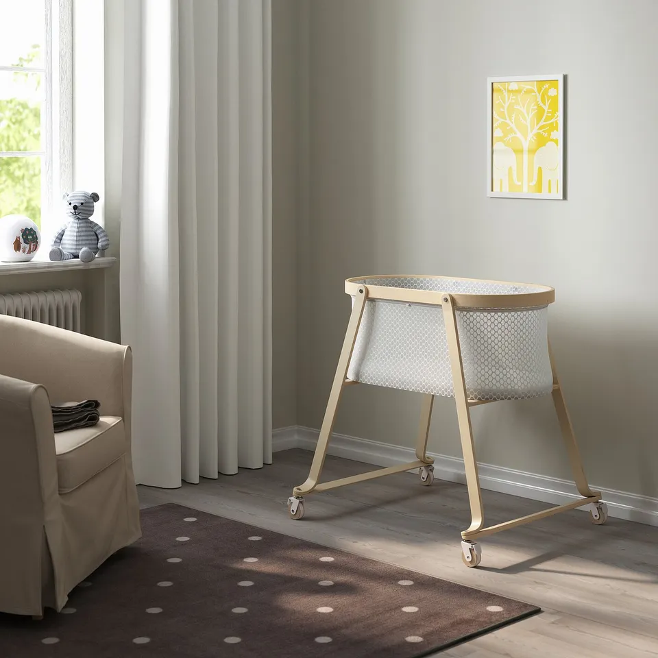 Modern nursery with ÄLSKVÄRD bassinet, polka-dot rug, beige chair, teddy bear, yellow frame.