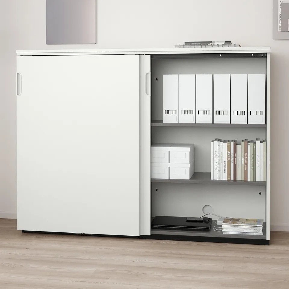 White storage cabinet with sliding doors, adjustable shelves holding files and books, and a lock for security.