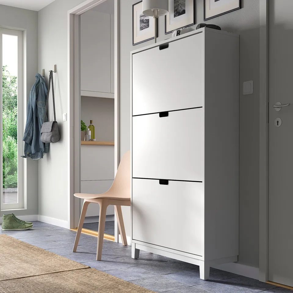 Modern entryway with white STÄLL shoe cabinet next to grey cabinet and door, chair nearby.