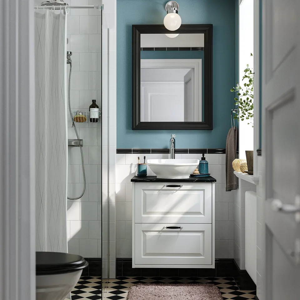 White sink cabinet with black counter, mirror, plants, towels, shower.