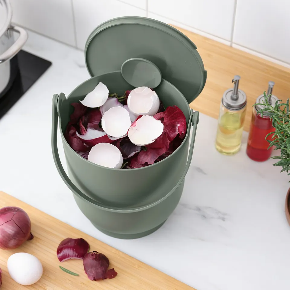 Green kitchen compost bin with lid holds food scraps; sits on countertop for easy access.