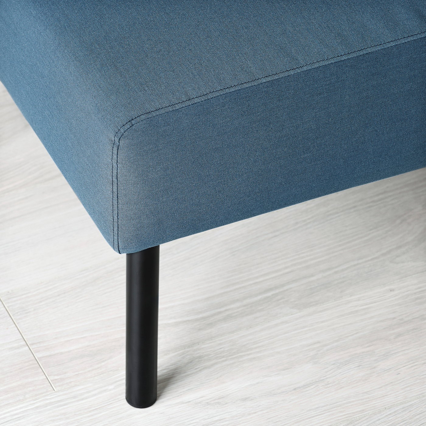 Blue fabric-covered footstool with black metal leg on a light wooden floor.