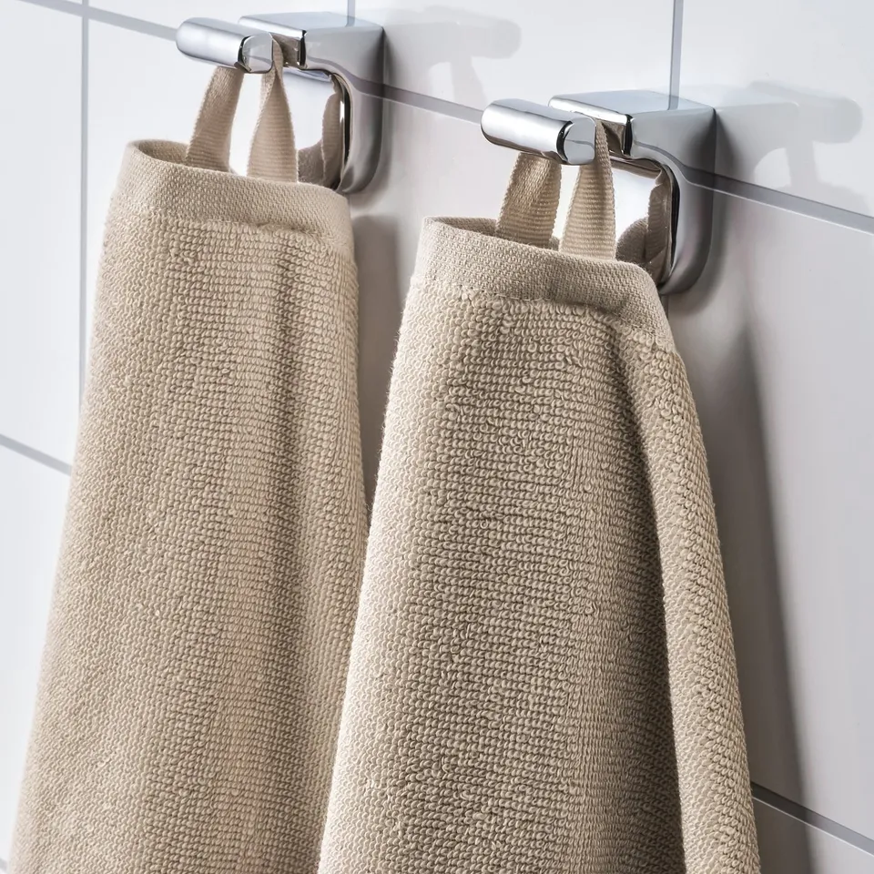 Two beige towels hang from metal hooks, showcasing absorbent terry texture and quick-drying stripes.