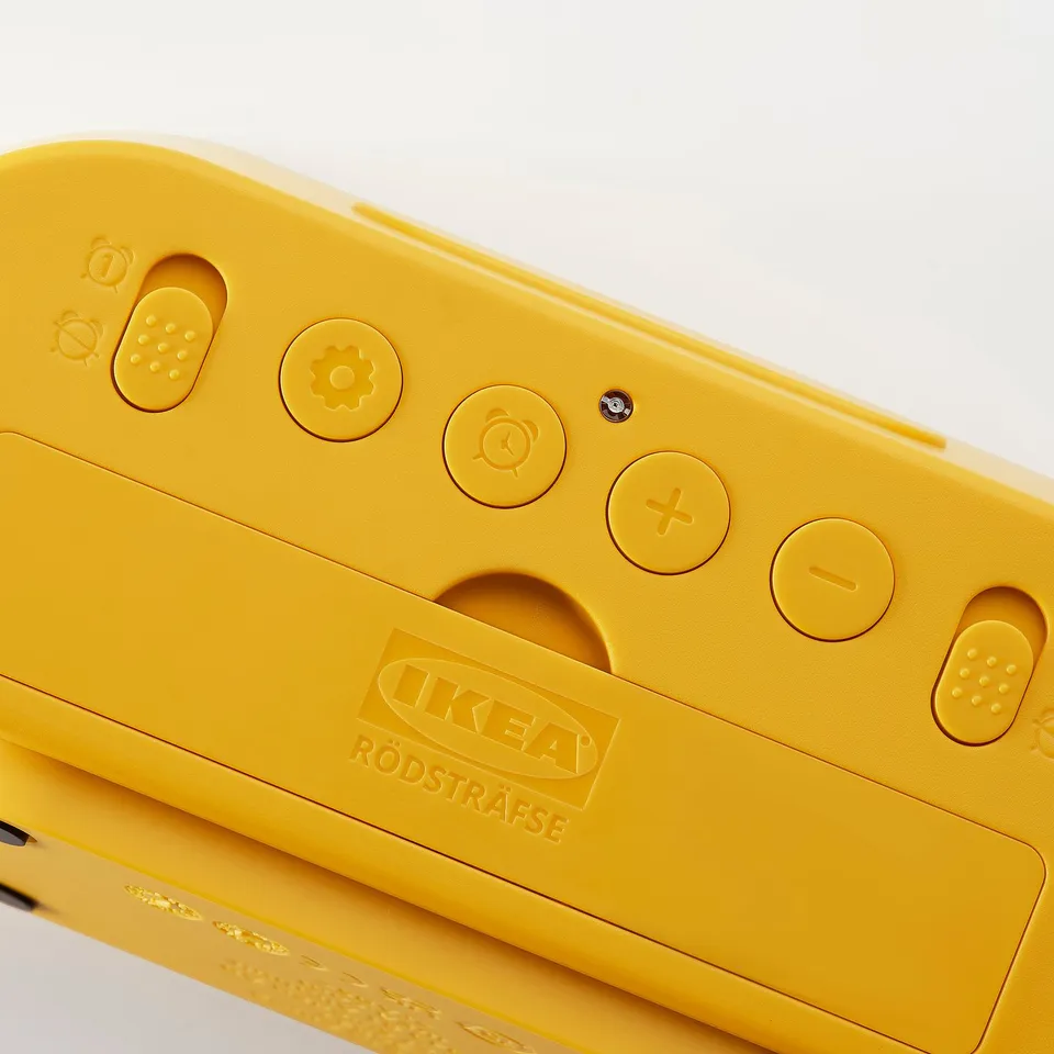 A bright yellow IKEA RÖDSTRÄFSE alarm clock with clear buttons and large screen displaying time and functions, versatile and practical design.