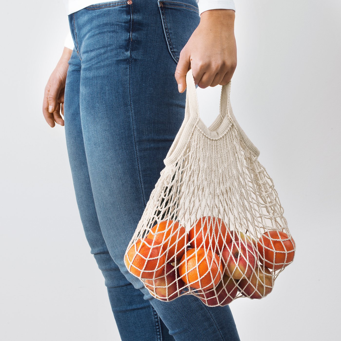 Person holding a mesh produce bag with oranges.