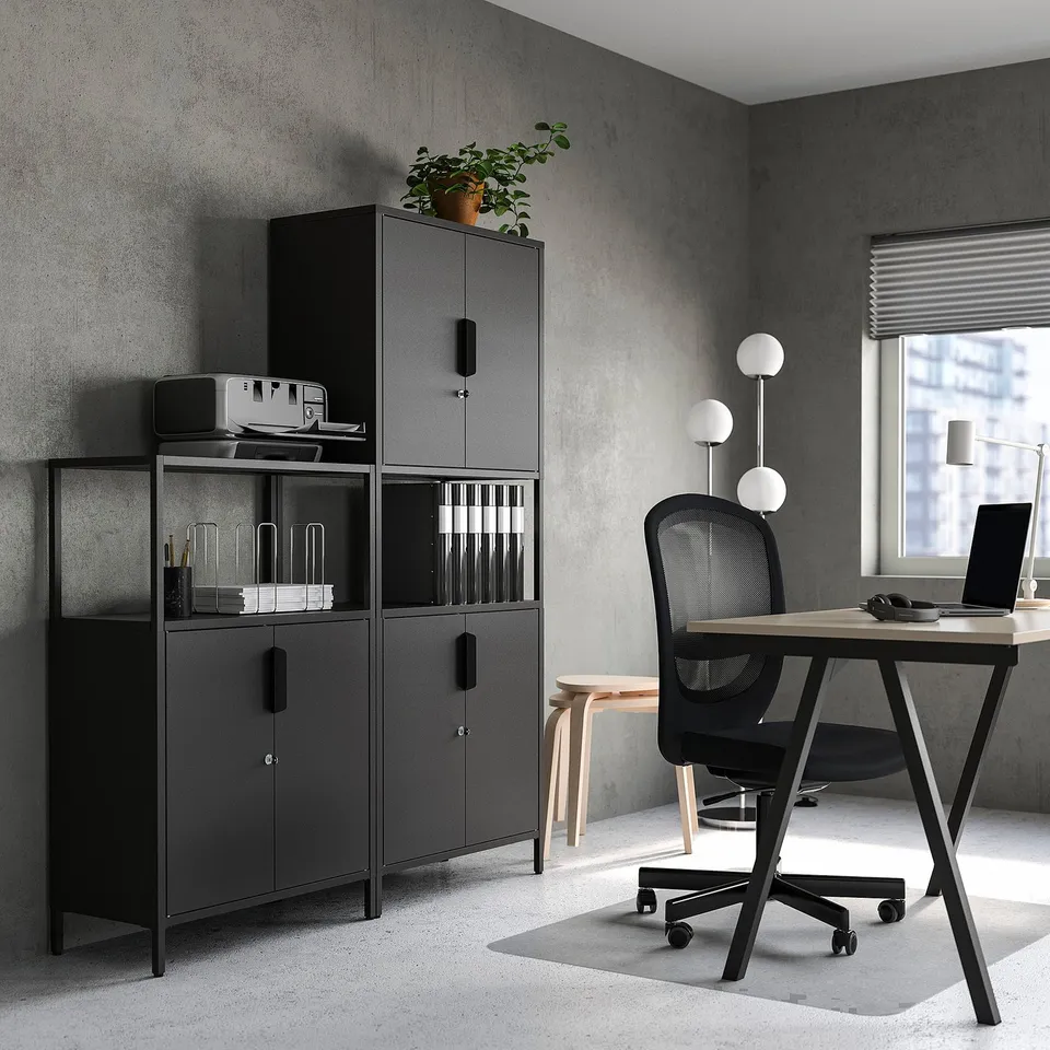 Modern office with black TROTTEN storage cabinet, lockable compartment, next to office chair and wooden desk, styled with stool and pendant lamp.