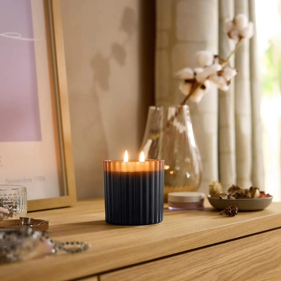 TOFSTÄRNA candle on wooden shelf with vase, bowl, and calendar. Dark blue glass, lit.