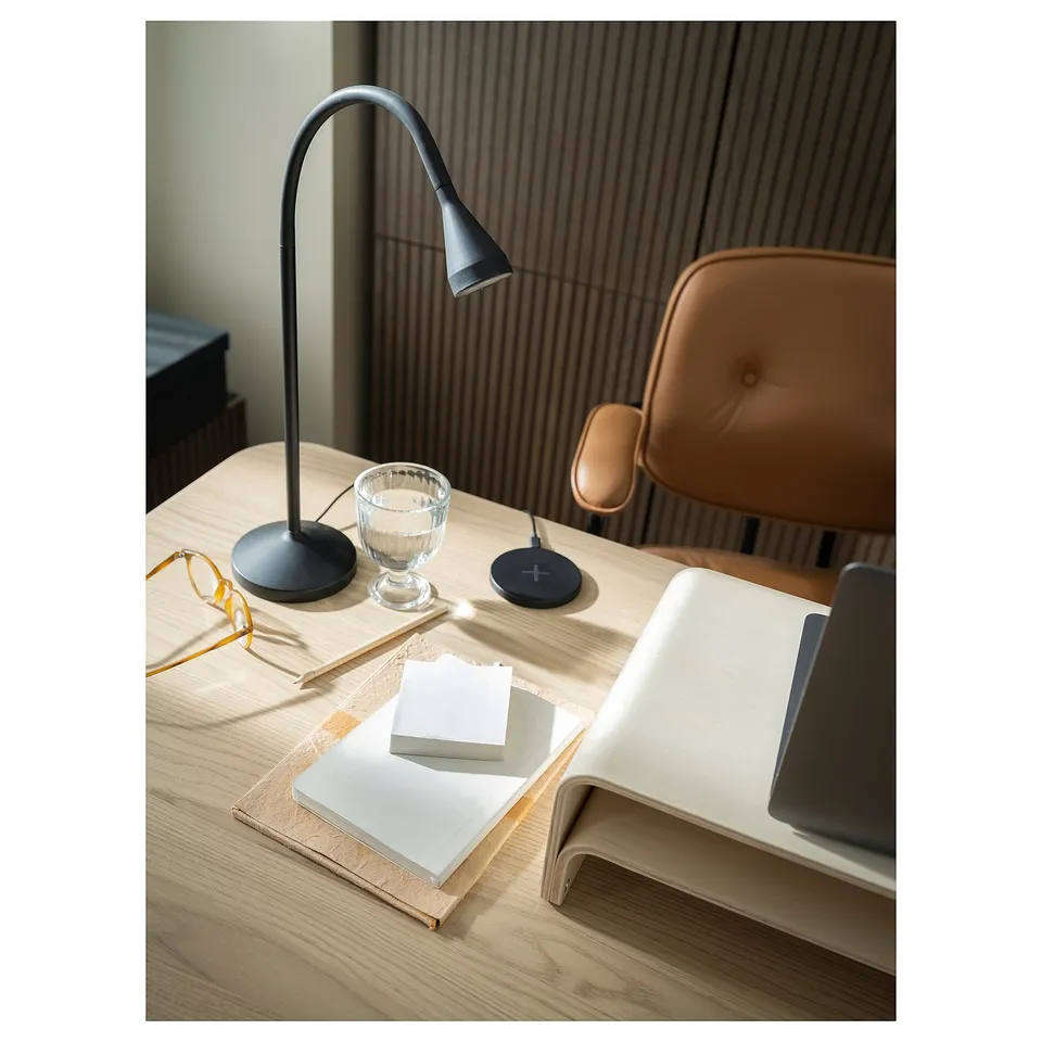 Black desk lamp, brown leather chair, wooden desk with open book, glass, & tech. Modern, sleek design.