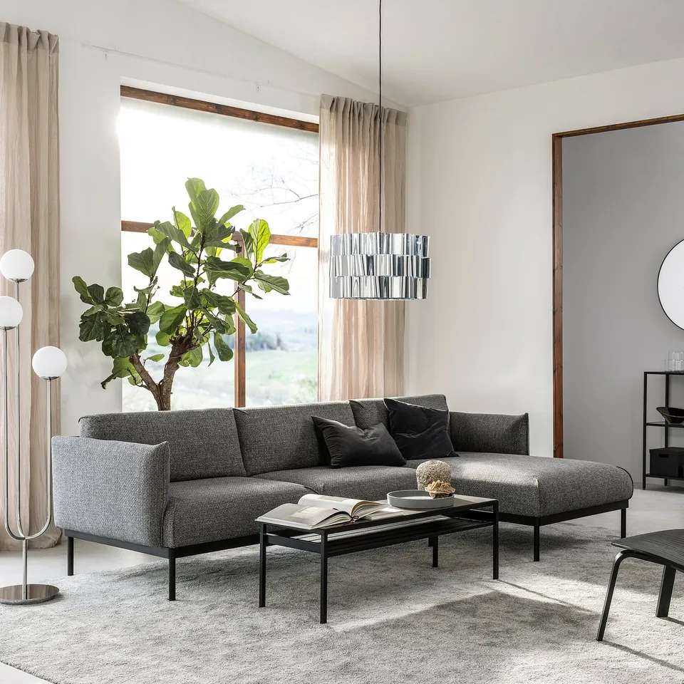 Modern living room with dark grey ÄPPLARYD sofa, black coffee table, large window with beige curtains, floor lamp, and stacked side tables.