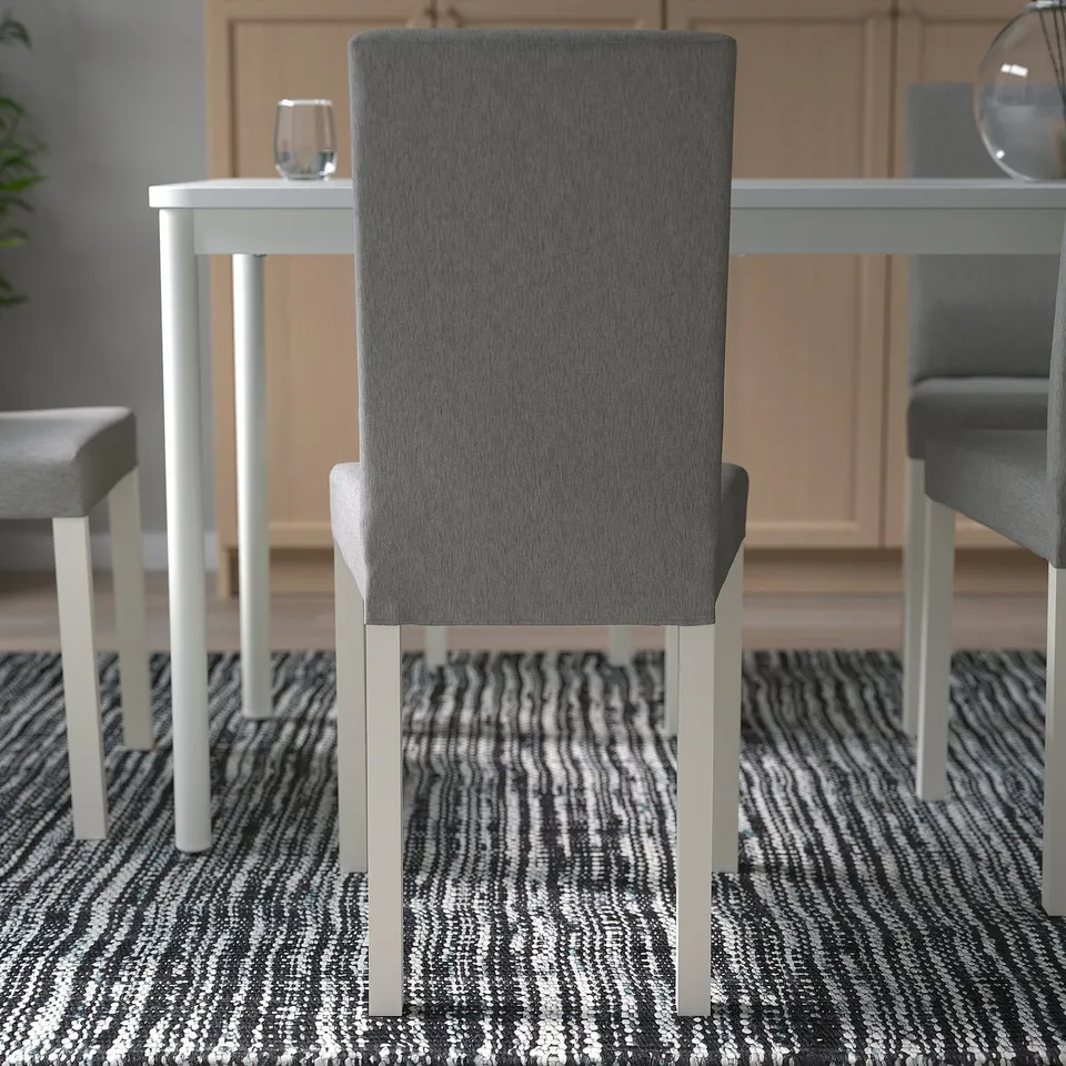 Modern chair with fabric seat and back, white legs, on striped rug, by table.