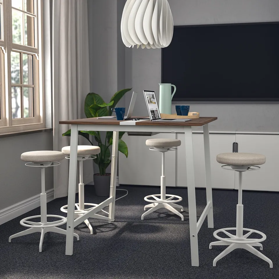 MITTZON high table setup with white stools, wooden top, and sleek design. Tables large, surrounded by smaller stools, near a window and plant.