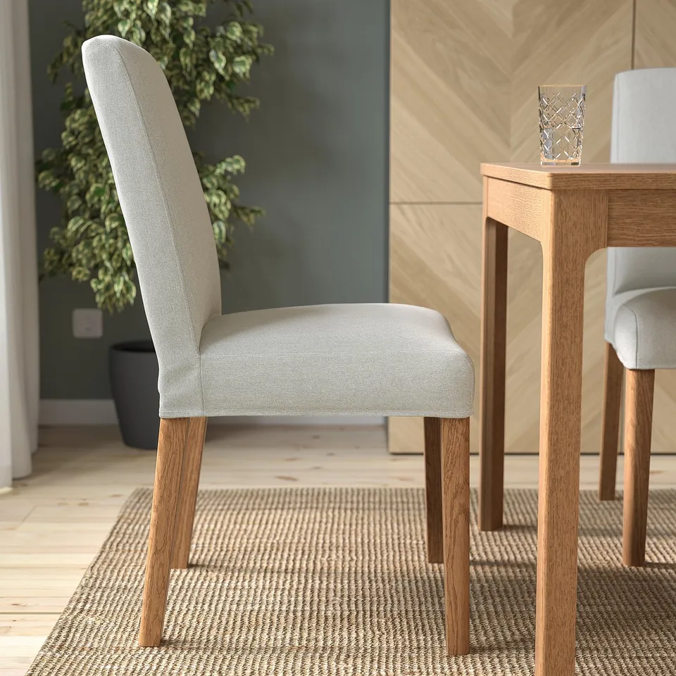 Modern dining chair with light grey upholstery and wooden legs near a table.