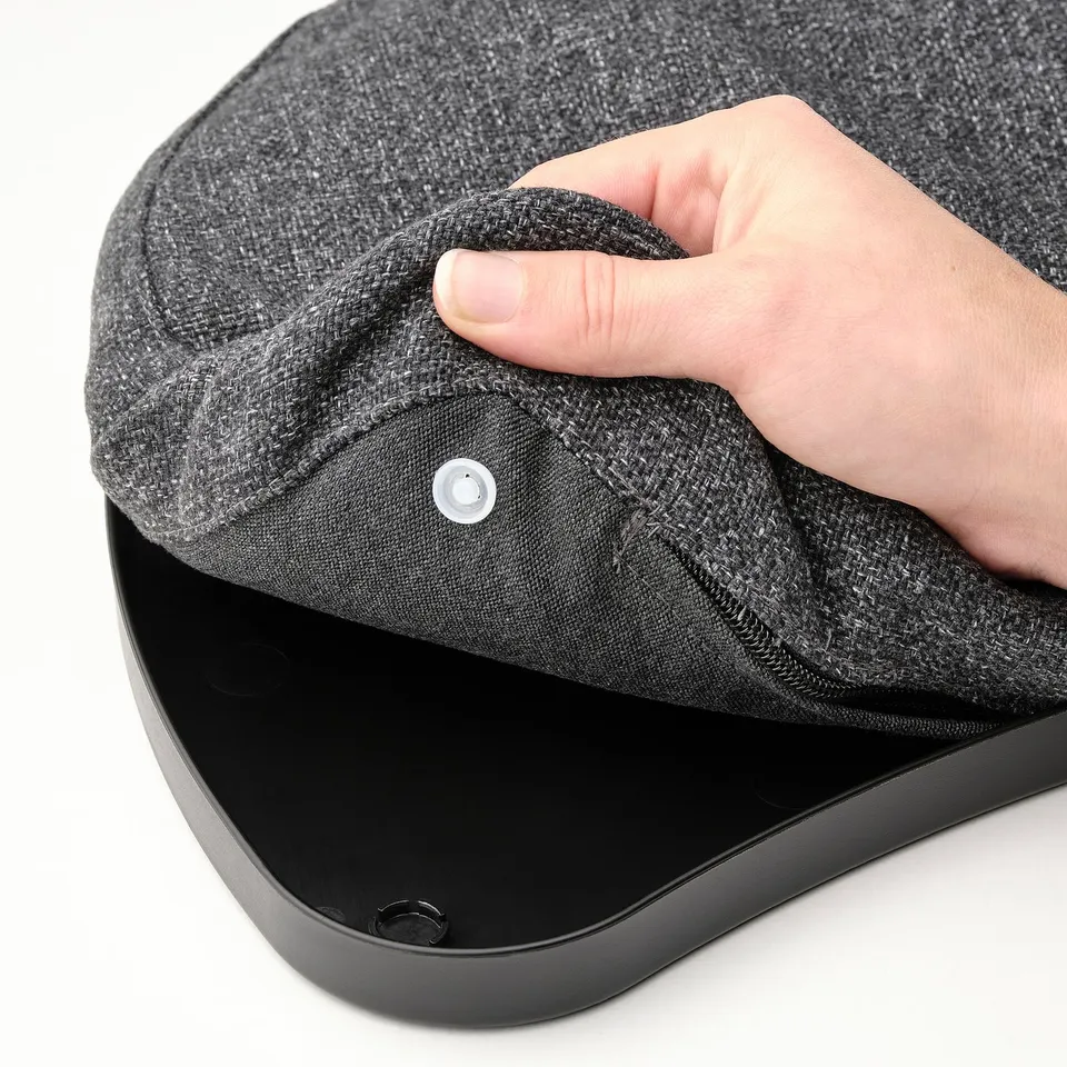 A hand placing a grey cushion with a removable cover on a black laptop stand.