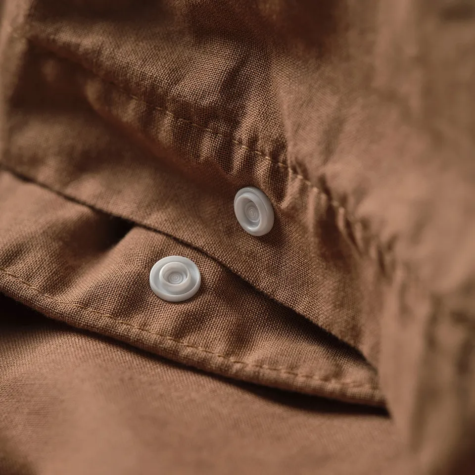 Close-up of a brown duvet cover with two white buttons, representing a simple and cosy design.