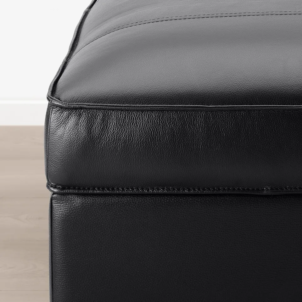 Black leather footstool with clean, precise stitching and smooth texture. Part of the KIVIK series, it exudes quality and comfort.