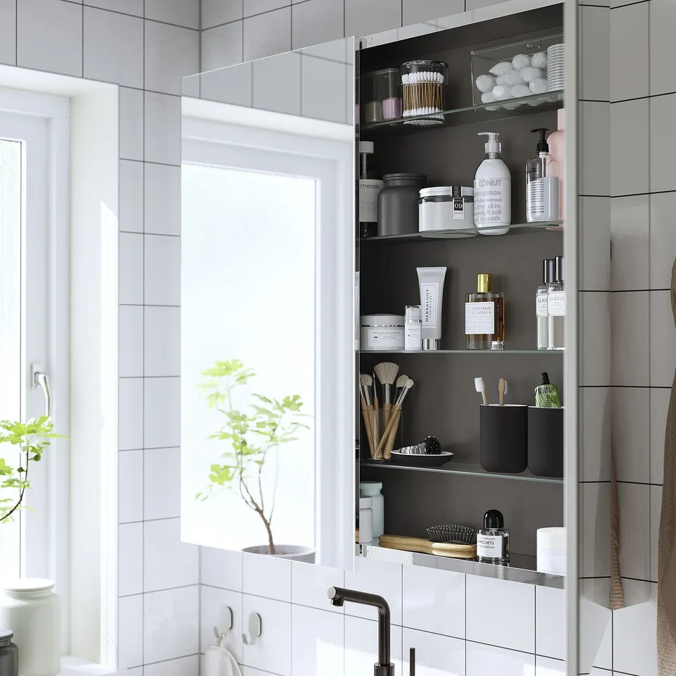 Mirrored cabinet with adjustable shelves, storing bathroom products and makeup.
