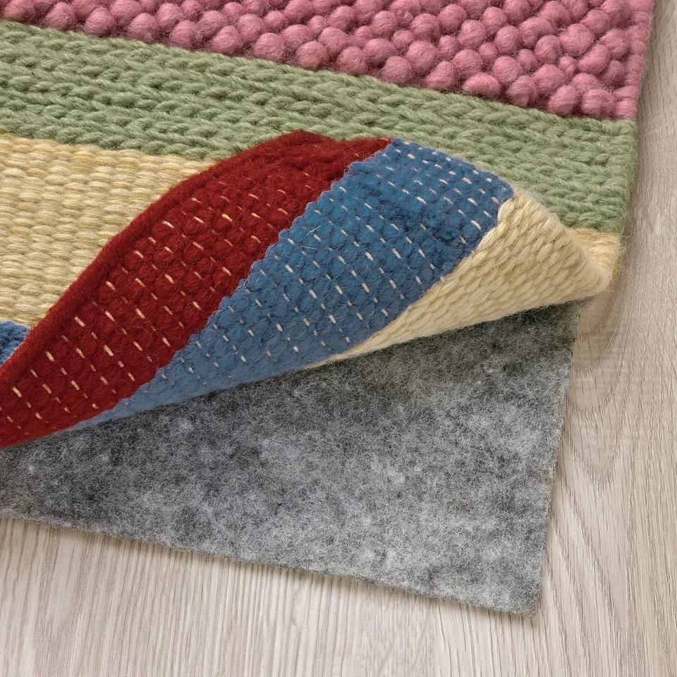 Colourful, handwoven rug showcasing vibrant patterns and textures, laid over grey felt backing on wooden floor.