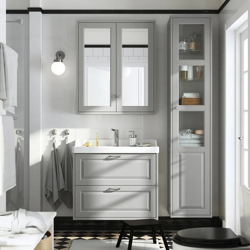 Modern grey bathroom with TÄNNFORSEN vanity, mirrored cabinet, hanging towels, and black stool. Vanity fits under tall cabinet, white countertop.
