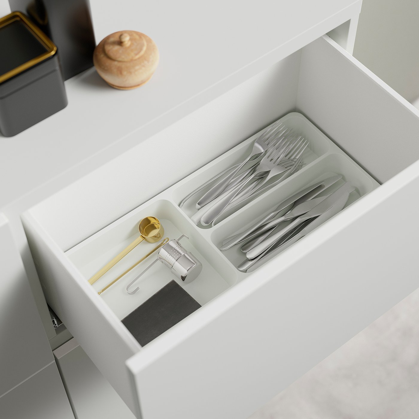 Open drawer with organised cutlery in compartments. Gold measuring spoon and canister visible.