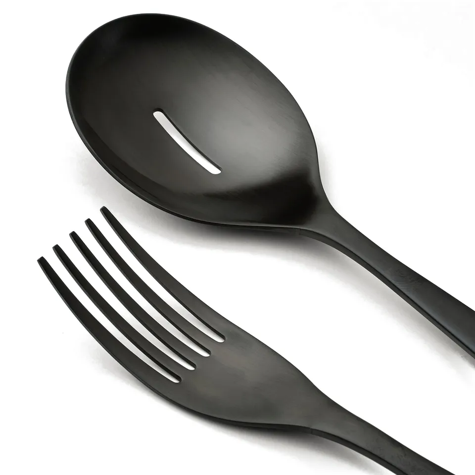 Black stainless steel serving spoon with holes and fork, placed together on a white surface. Sleek and modern design.