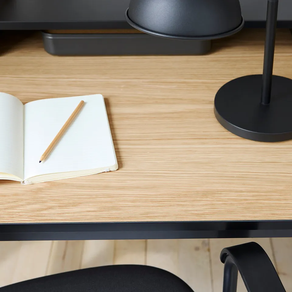 Minimalist home office setup with light wood desk, open notebook, and sleek black chair.
